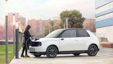 אישה מחברת את הונדה e החשמלית לעמדת טעינה לרכב חשמלי