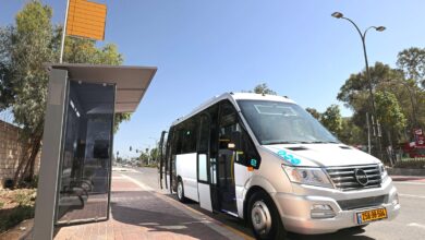 מיניבוס חשמלי בצבע אפור כסוף בהיר של QEV עומד לצד תחנת אוטובוס בירושלים