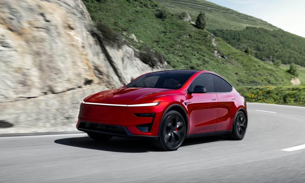 טסלה מודל Y פרפורמנס אדומה בנסיעה על כביש ההררי מפותל בין הרים ירוקים